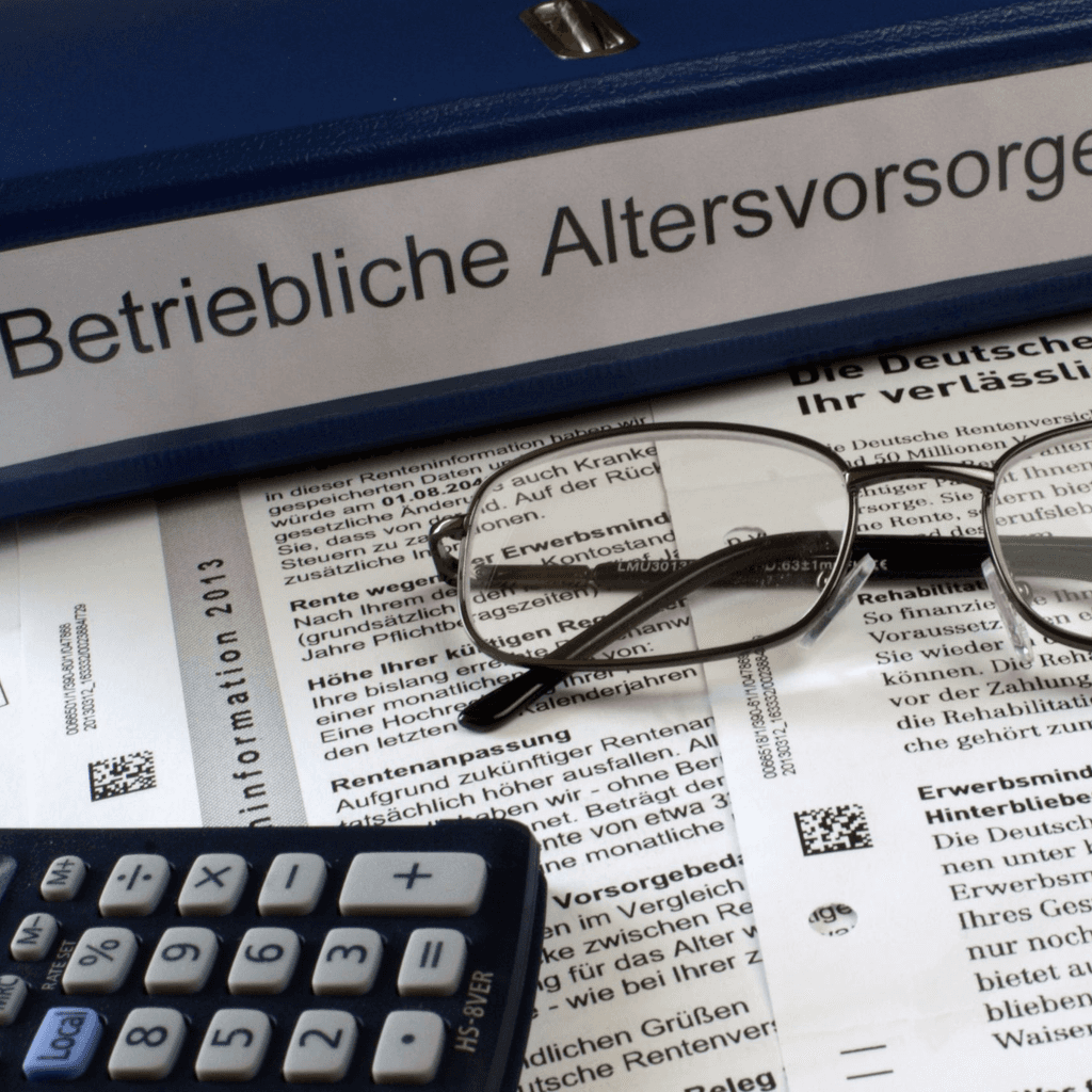 Binder labeled “Betriebliche Altersvorsorge” (company pension) with glasses and a calculator in front of it